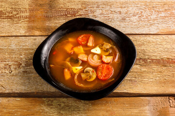 Traditional Thai Tom Yam soup in a black plate on a wooden table. Copy space