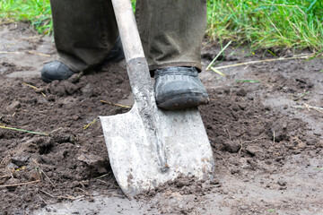 farmer, worker man digging soil, ground with shovel in rubber boots in garden, close up