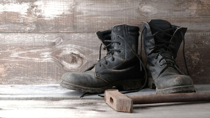 Old dirty shoes boots boots and hammer on a wooden background