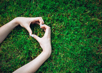 Female hands making a heart sign with fingers, on grass background. Love concept for valentines day.