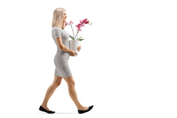 Full length profile shot of a young woman walking a carrying an orchid flower pot