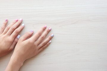 Stylish trendy female pastel white, pink and blue manicure. Beautiful young woman's hands on wooden background. Copy space banner