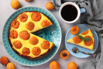 Cheesecake with apricots with a cut out piece, located on a blue plate and cup of coffee, Top view