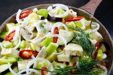 Vegetables and meat for barbecue. Stew of vegetables and meat in a frying pan with a handle and a wooden board. Close up and black wooden background.