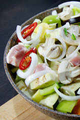 Vegetables and meat for barbecue. Stew of vegetables and meat in a frying pan with a handle and a wooden board. Vertical image and black wooden background.