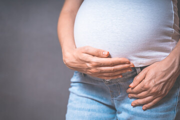 Pregnant woman holds hands on belly on a gray background. pregnancy, motherhood, people and expectation concept. Close-up, copy space, indoors. Toned photo of pregnancy.