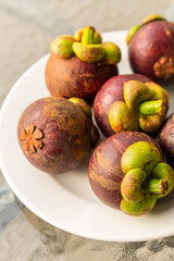 White plate full of mangosteen fruit with fresh leaves close-up vertical photo