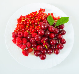 Assorted red fresh berries on a plate on a white background.