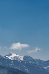 Fototapeta na wymiar Two paragliders are flying over a mountains in Bavaria on background of blue sky with clouds in spring sunny day. Vertical wallpaper