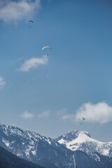 Three paragliders are flying over a mountains in Bavaria on background of blue sky with clouds in spring sunny day. Vertical wallpaper