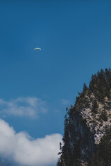 Paraglider flies over a mountain in Bavaria on background of blue sky with clouds in spring sunny day. Vertical wallpaper