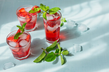 Fresh strawberry cocktail. Summer pink cocktail with strawberry, green mint leaves and ice cubes on light blue background mockup. Trendy shadows and sunlight background with copy space for text.