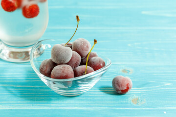 frozen cherry berries in a glass bowl on a blue wooden background, horizontally. Copy spaces