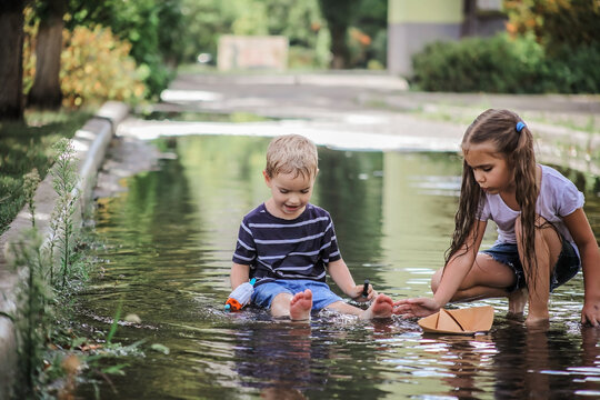 Cute happy kids playing with paper boat in the puddles after warm summer rain, lifestyle outdoor