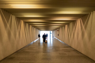 people walking down an airport corridor with yellow walls with a set of lights on the ceiling and...