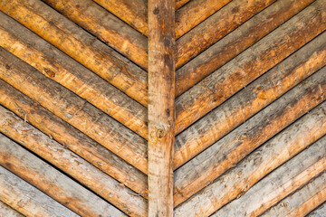 A cottage exterior wall made of wooden logs with texture and wood knots. Fragment of unpainted and debarked logs barn or cabin wall background