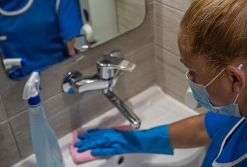 A cleaning leady with the mask on her face cleans the washbasin