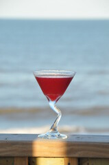 Chilled Pomegranate Martini  on a deck railing with the beach and ocean in the background.
