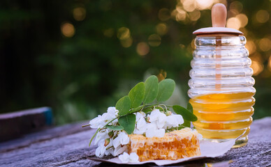 Acacia natural liquid honey in transparent jar on wooden table next to honey comb and branch of white acacia.