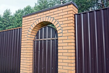 brown metal fence wall with closed door and brick arch on the street