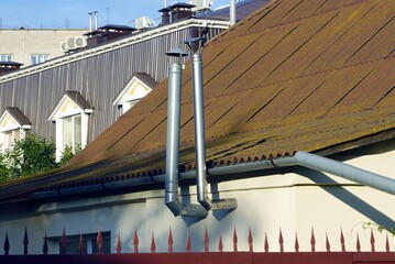 two gray metal chimney pipes on the wall of the house near the brown slate roof