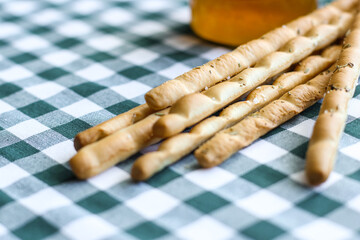 Breadsticks or Italian grissini snack with jar of honey on green gingham tablecloth. Food, harvest concept. 