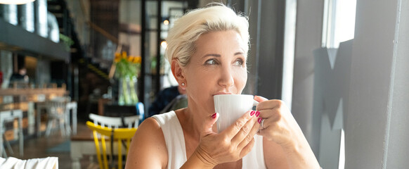 Mature woman drinking a cup of coffee in cafeteria.