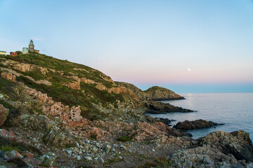 Fototapeta na wymiar Lighthouse with full moon after sunset during summer season at Kullaberg nature reserve in south Sweden. Selective focus.
