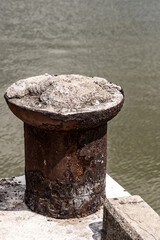 Naklejka premium metal mooring element is an old rusty metal bollard on the edge of the pier against the background of water