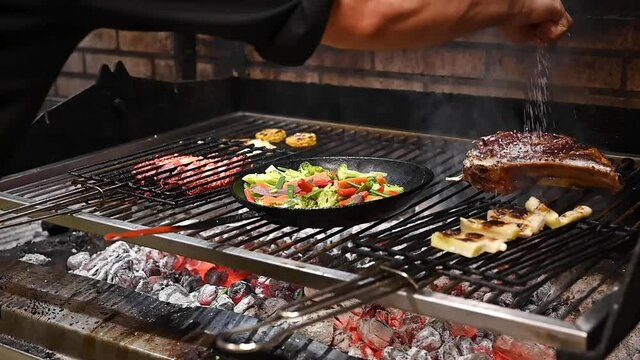 Close up view of hand of male chef adding salt to delicious meat steak on hot grill while cooking it. High quality FullHD footage