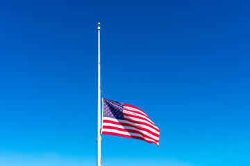 Flag of the United States flying at half staff waving in the wind under blue sky
