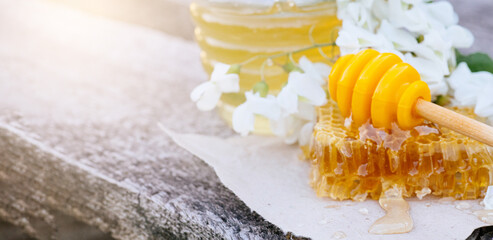Pouring honey into jar of honey from Honey Dipper, Stick. Acacia honey in gar on wooden background. Spring mood. Selective focus.