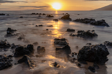 Sunset on beach in Hawaii Maui Long exposure of waves coming in over sharp rocks. 