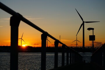 Fototapeta na wymiar Beautiful sunset at jetty over the water with windmills and industrial shipping. 