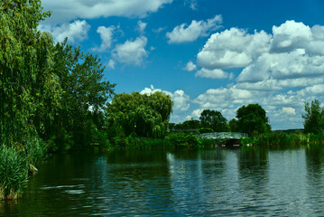 A bridge connecting between two islands in a river with many trees on the river bank with a background of blue sky with clouds in a summer sunny day