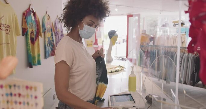Store owner in clothes store scanning clothes label with barcode reader wearing protective face mask during Covid-19 Pandemic