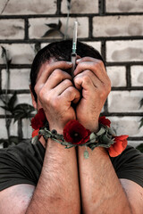 addiction concept: addict with a syringe, his hands tied with poppy stems and flowers, increased contrast, soft focus