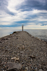 Fototapeta na wymiar Lighthouse on a stone spit against the backdrop of a bright blue sky