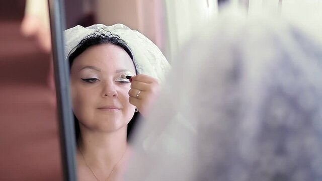A Jewish bride wears makeup in front of a mirror before the chuppah ceremony.