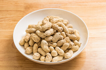 A plate of salted, dried peanuts in the shell on a wood-grain desktop