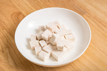 A dish of neatly cut taro pieces on a wood-grain table