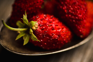 Red ripe wild strawberry in old vintage spoon on the rustic background. Selective focus. Shallow depth of field.