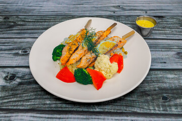 A plate of rice with vegetables and salmon skewers.