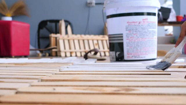 Hands of a man painting white color to a wooden fence, selective focus shallow depth of field