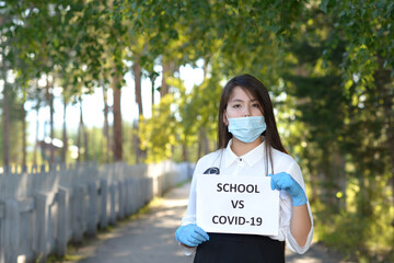 A schoolgirl wearing a medical mask against a green tree. A high school student stands in a school alley. A girl in an mask and medical gloves holds a leaflet with an inscription.