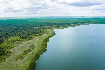 summer countryside landscape with blue lake and green forest under cloudy sky. aerial photography with drone