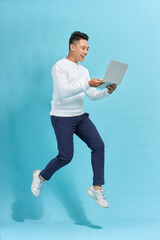 Full length portrait of happy man jumping and holding  laptop isolated over blue background