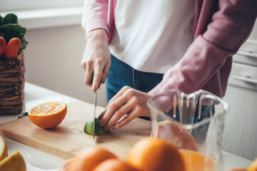 Close up photo of a caucasian woman with red hair and freckles slicing a lime and orange while making fresh juice at home