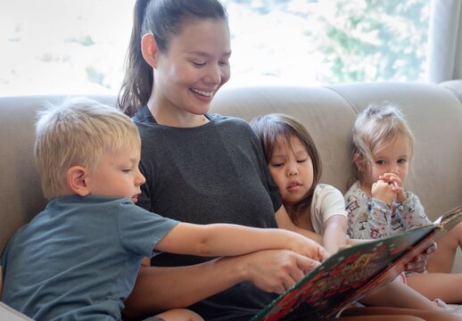 A woman reading a story book to young kids. Teaching children at home.