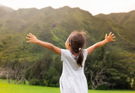 Happy people in nature. Little girl standing outside, arms raised.